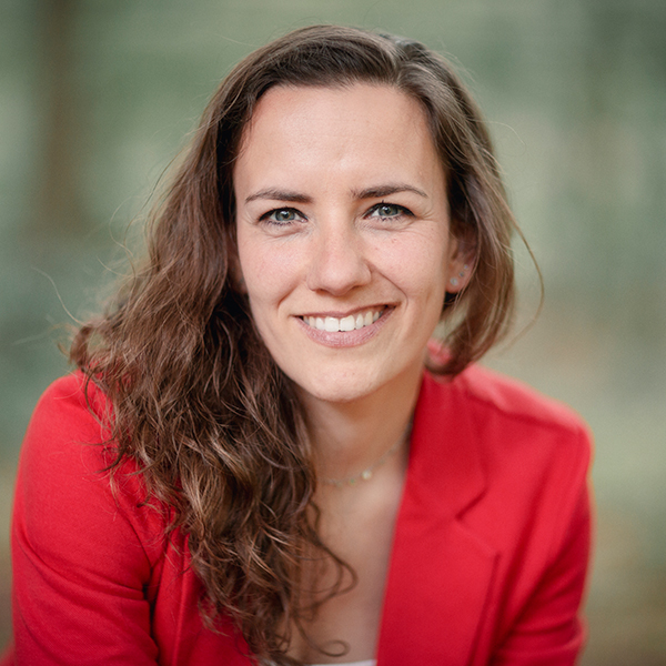 Alicia Zuiderwijk zit buiten met een grote glimlach en een rood pakjasje aan